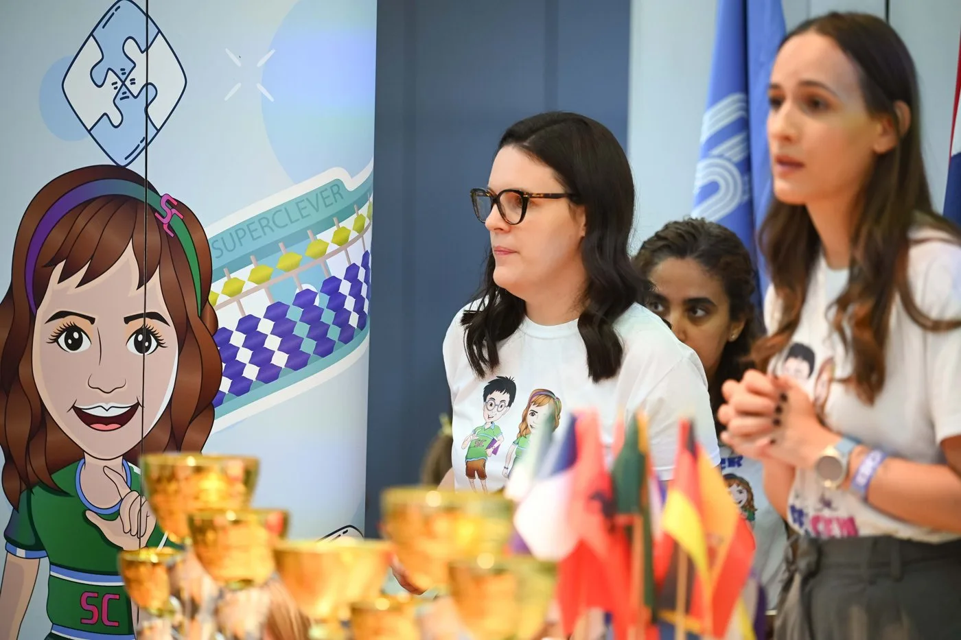 Voditeljice Superznalac centara na Međunarodnoj olimpijadi, uz pehare i zastave zemalja mreže