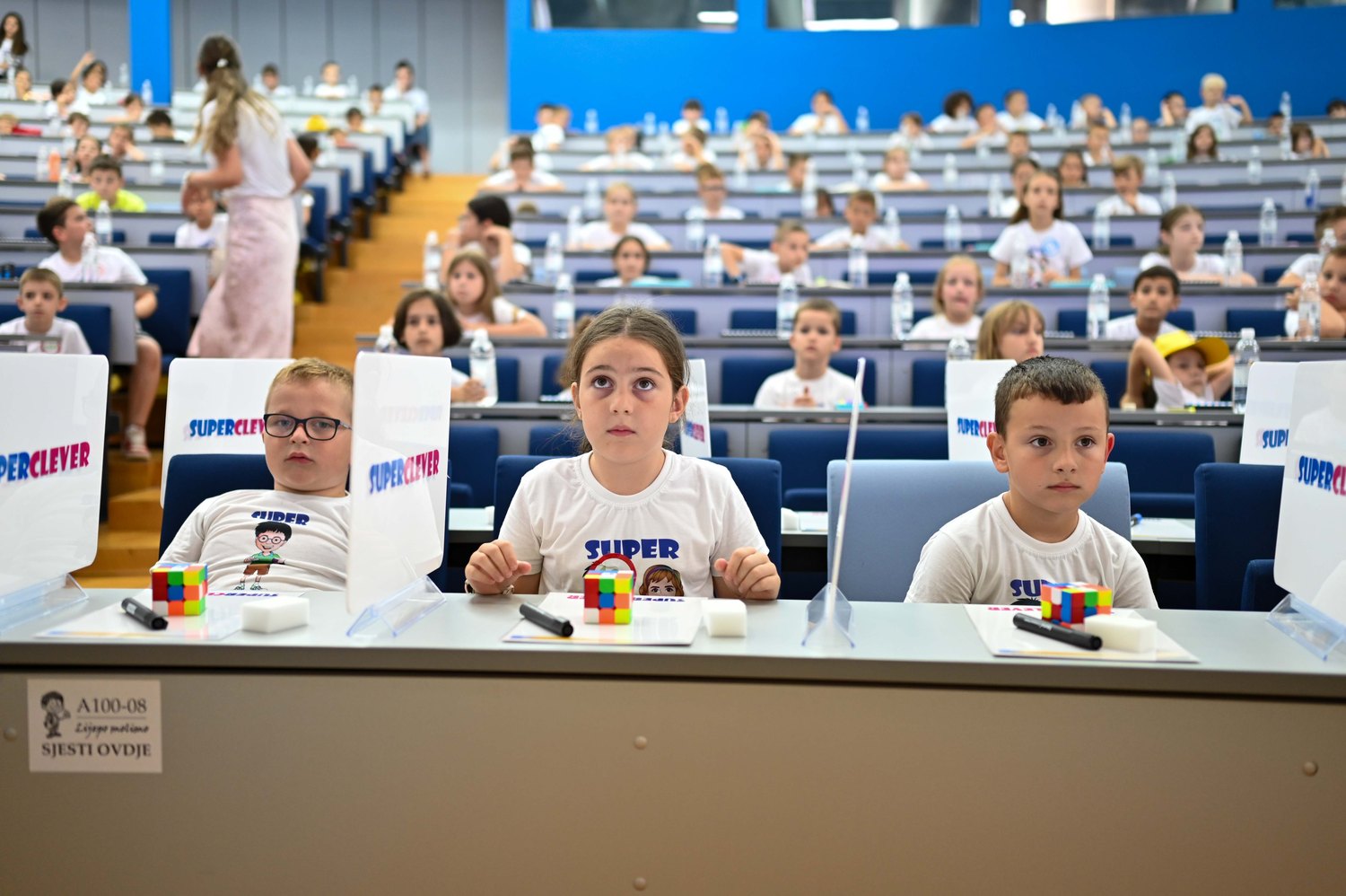 Troje natjecatelja za stolom, ispred njih Rubikove kocke
